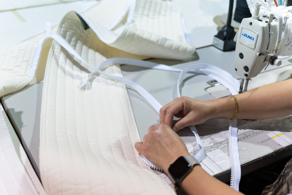 Person working on a sewing machine with a white garment of a Sprout Mattress