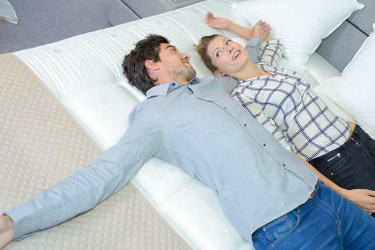 man and woman laying down on mattress in a showroom
