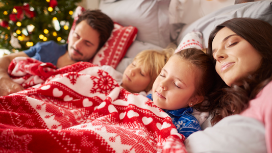 family of four sleeping together under a blanket on the couch, holiday sleep guide