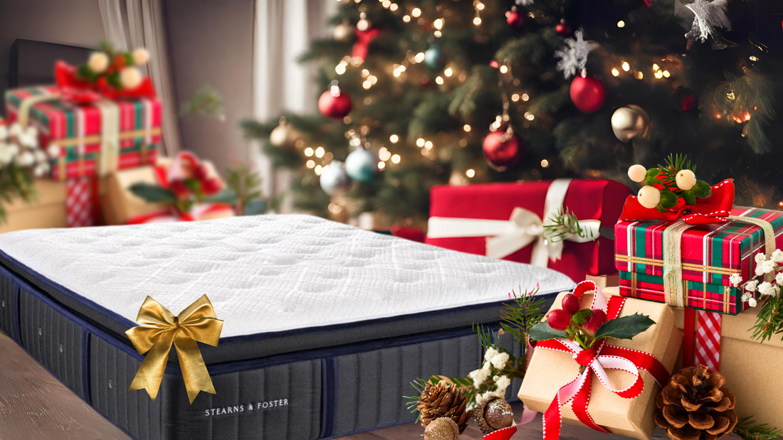 A mattress with a gold bow beside a decorated Christmas tree and wrapped gifts.