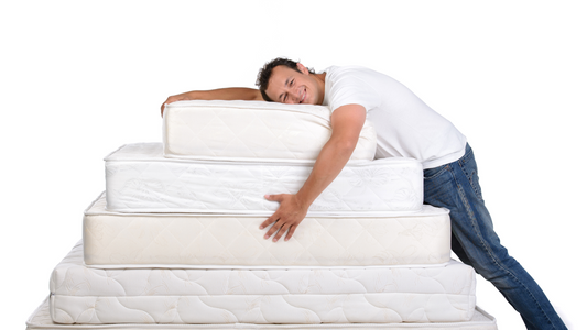a man leaning against and hugging a stack of mattresses formed from various mattress sizes into a pyramid shape