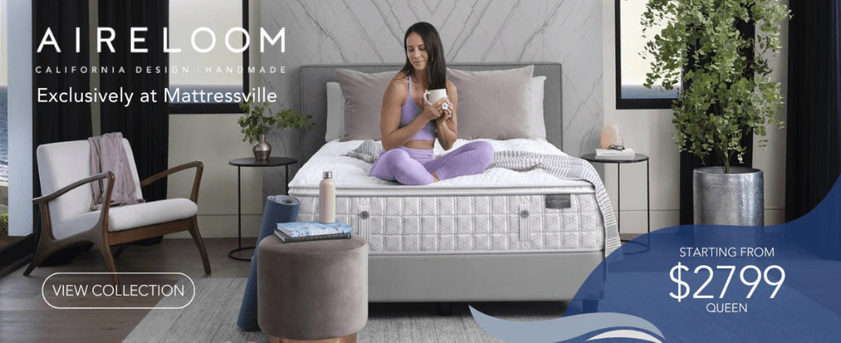 Woman in purple activewear sits cross-legged on a stylish bed, holding a mug. Modern room with a cozy chair, plants, and pillows. Mood is serene.