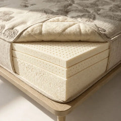 Close-up of a Natura Eco Brilliance mattress with visible layers of latex and a quilted top cover on a wooden bed frame.