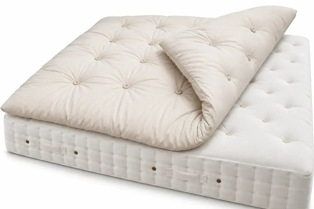 Alpaca tufted mattress topper in a warm cream or off-white color, shown partially rolled over a Helmsley Hypnos mattress on a clean white background.