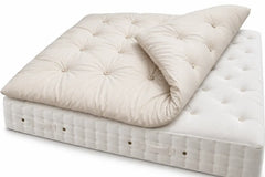 Alpaca tufted mattress topper in a warm cream or off-white color, shown partially rolled over a Helmsley Hypnos mattress on a clean white background.