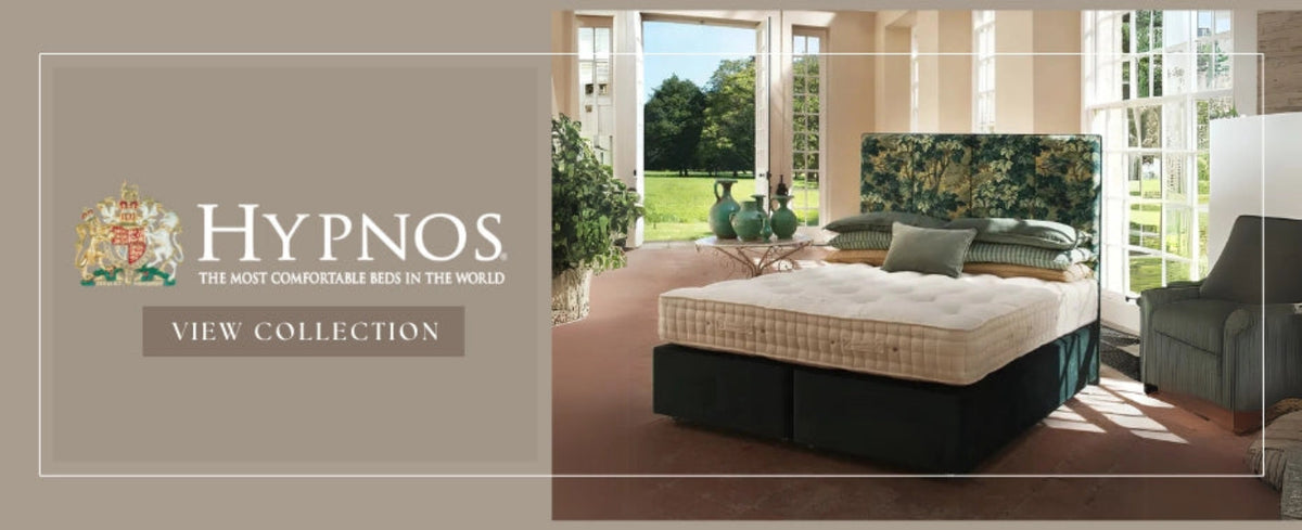 Luxurious bedroom with a plush bed and floral headboard, bathed in natural light from French doors opening to a lush garden. Text reads "Hypnos: The Most Comfortable Beds in the World."