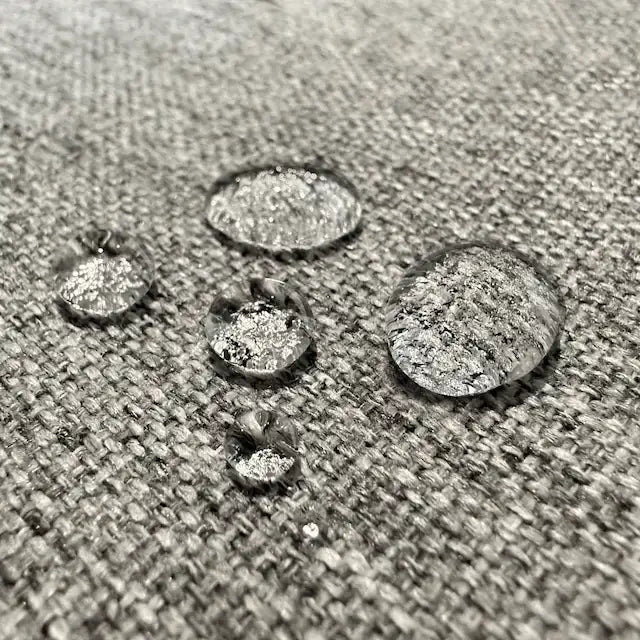 Close-up of water droplets beading on a gray Orthex waterproof fabric surface.