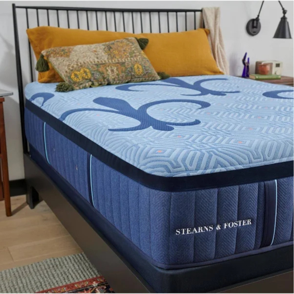 Navy Blue S&F Londynn Hybrid mattress with decorative pattern on a bed in a bedroom setting, featuring the Stearns & Foster brand.