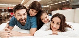 a family of four laying on a mattress in a mattress store smiling